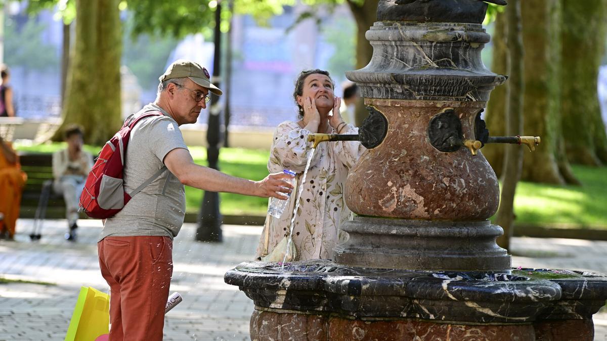Dos personas se refrescan en una fuente de Bilbao.