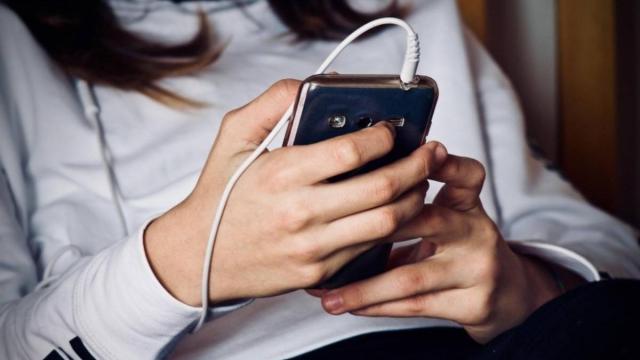 Una adolescente mira la pantalla de su teléfono móvil.