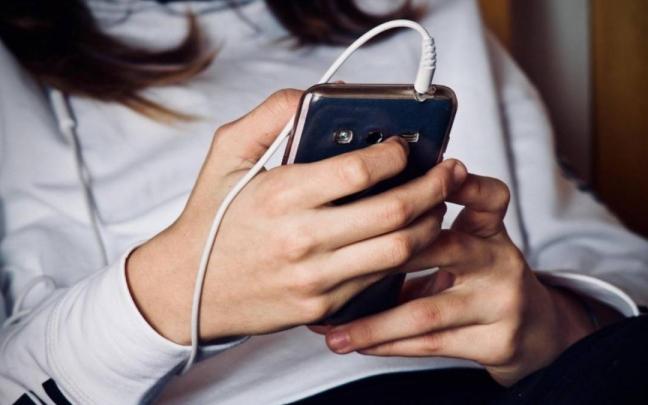 Una adolescente mira la pantalla de su teléfono móvil.