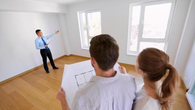 Una pareja, plano en mano, escucha las explicaciones de un agente inmobiliario.