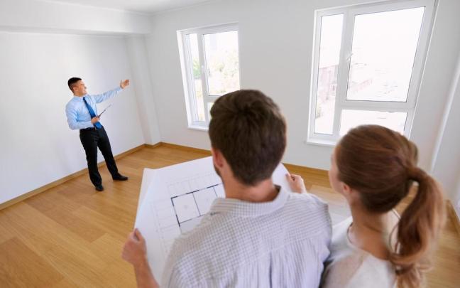 Una pareja, plano en mano, escucha las explicaciones de un agente inmobiliario.