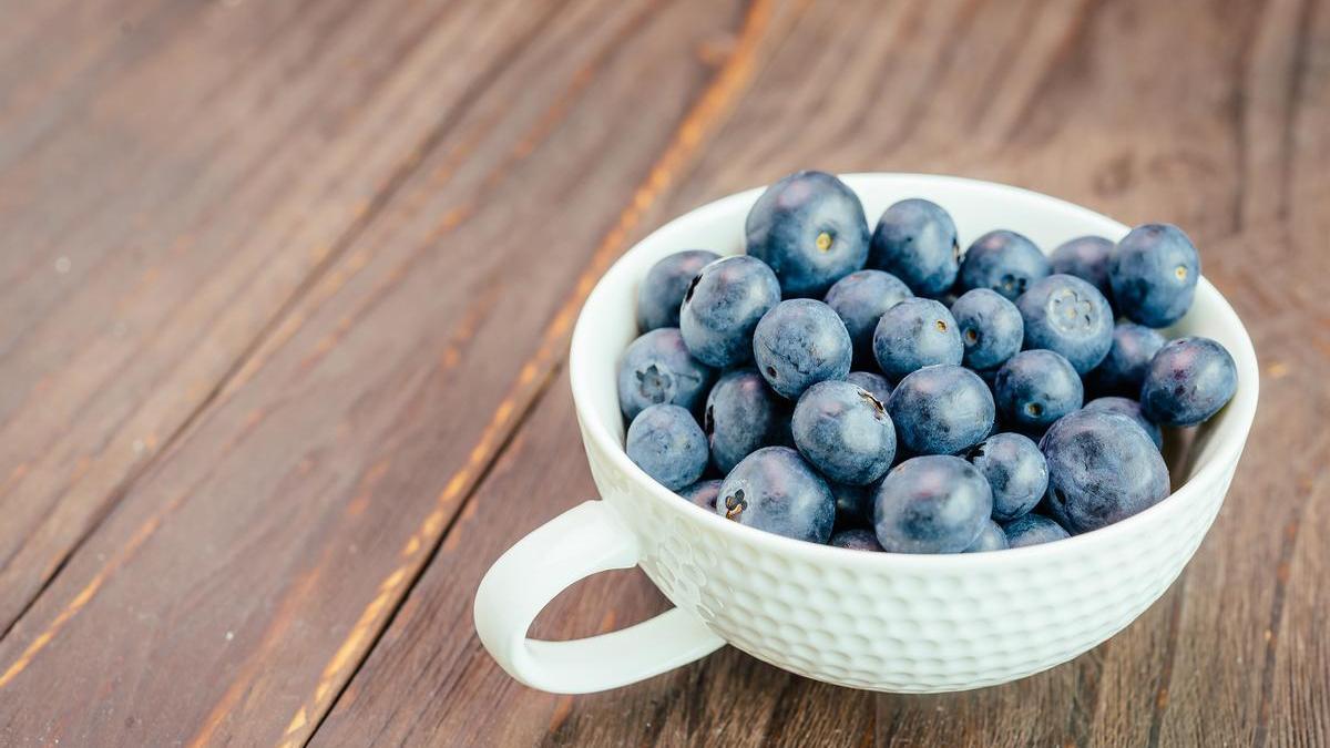 Taza blanca con arándanos sobre una mesa de madera