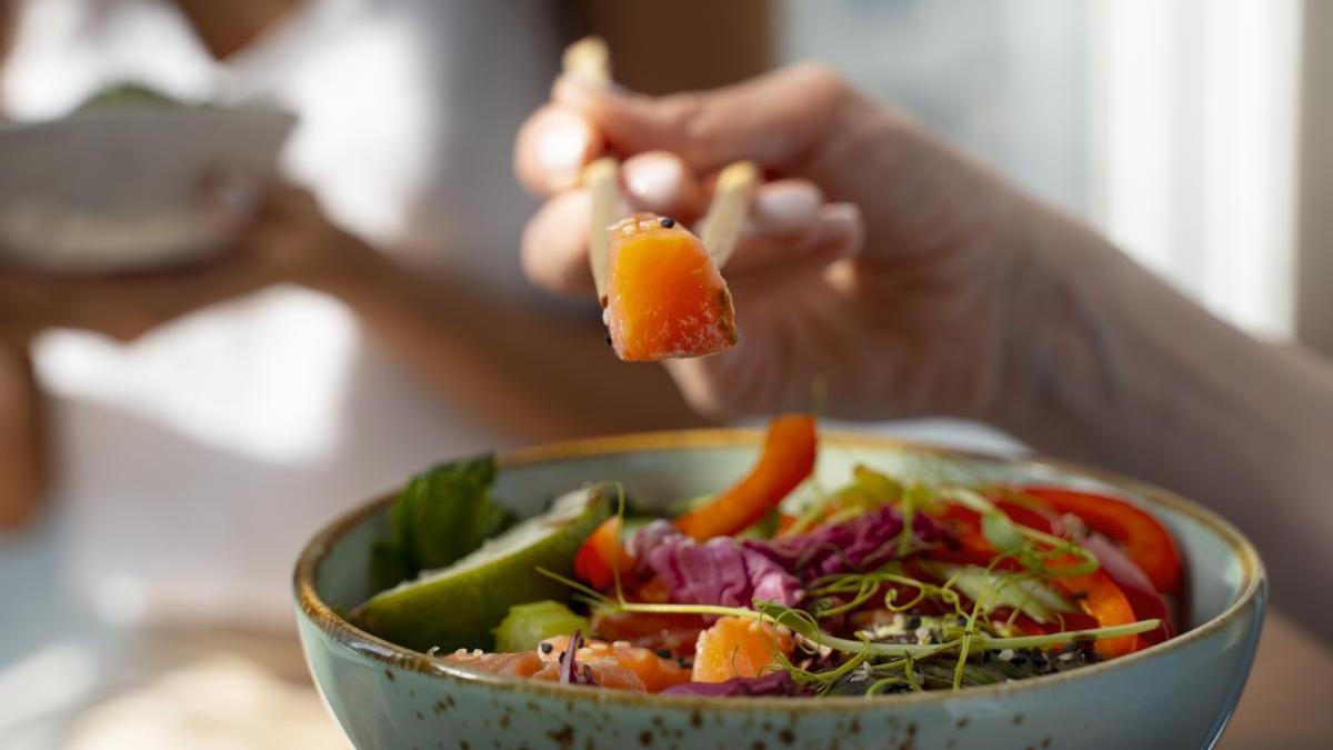 Manos de una chica disfrutando de un bol con salmón y diferentes alimentos saludables