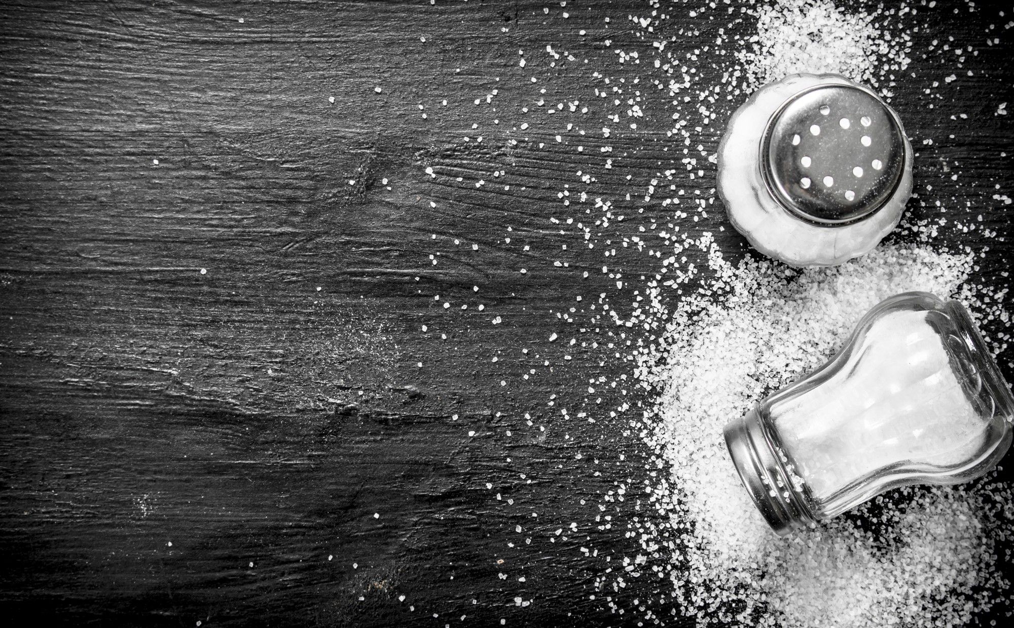 Dos saleros y sal derramada sobre una mesa de pizarra.