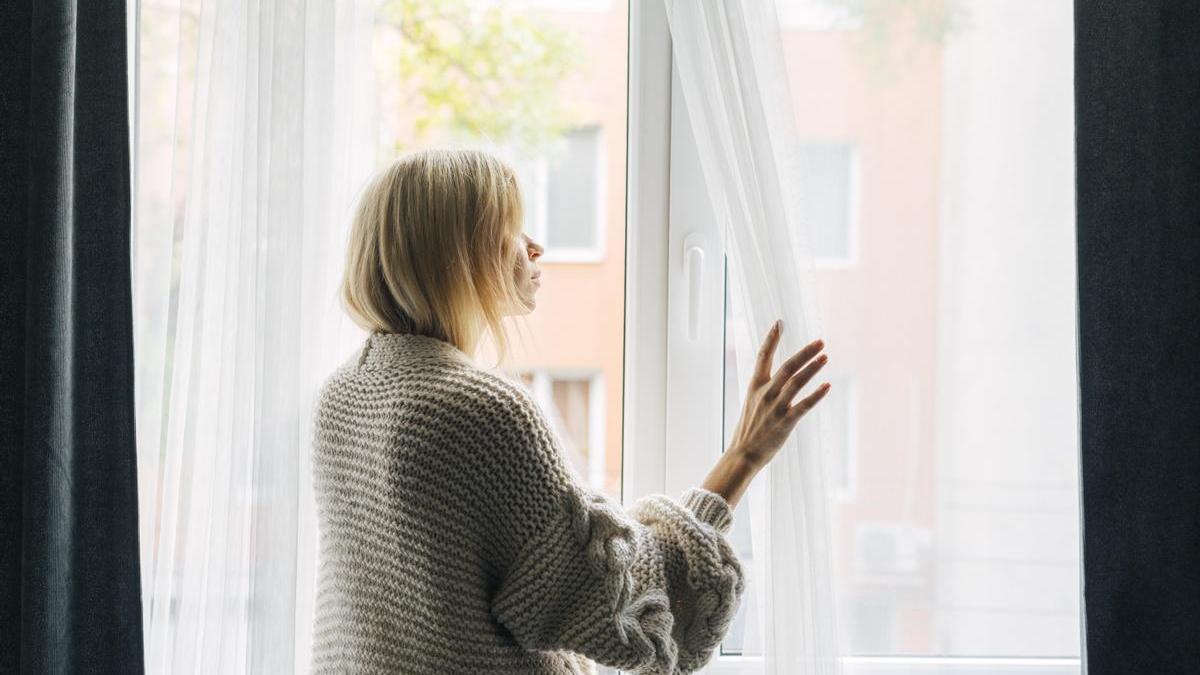 Joven aparta las cortinas para mirar por la ventana