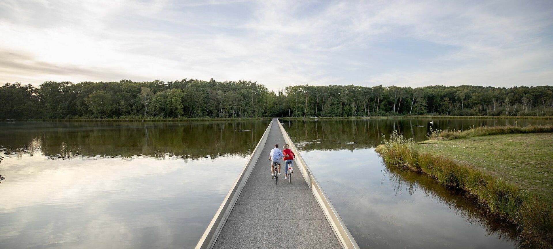 Dos ciclistas avanzan por el lago con el agua al ras del muro de hormigón.