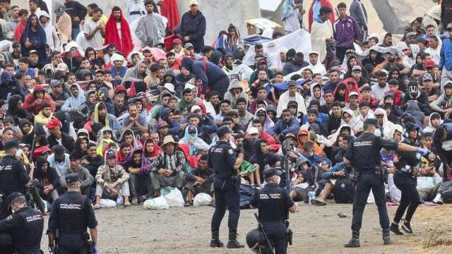 Agentes de Policía vigilan a migrantes que permanecen en la playa del Trampolín, en Ceuta.
