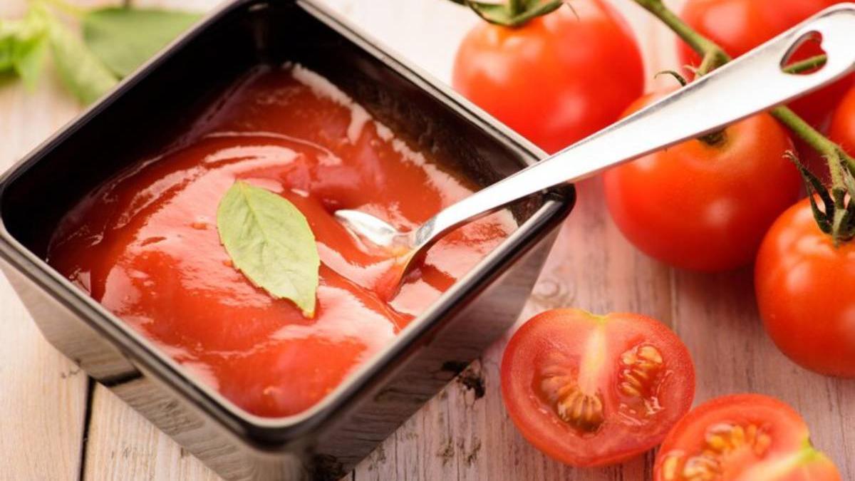 Tomate triturado natural en un recipiente al lado de varios tomates.
