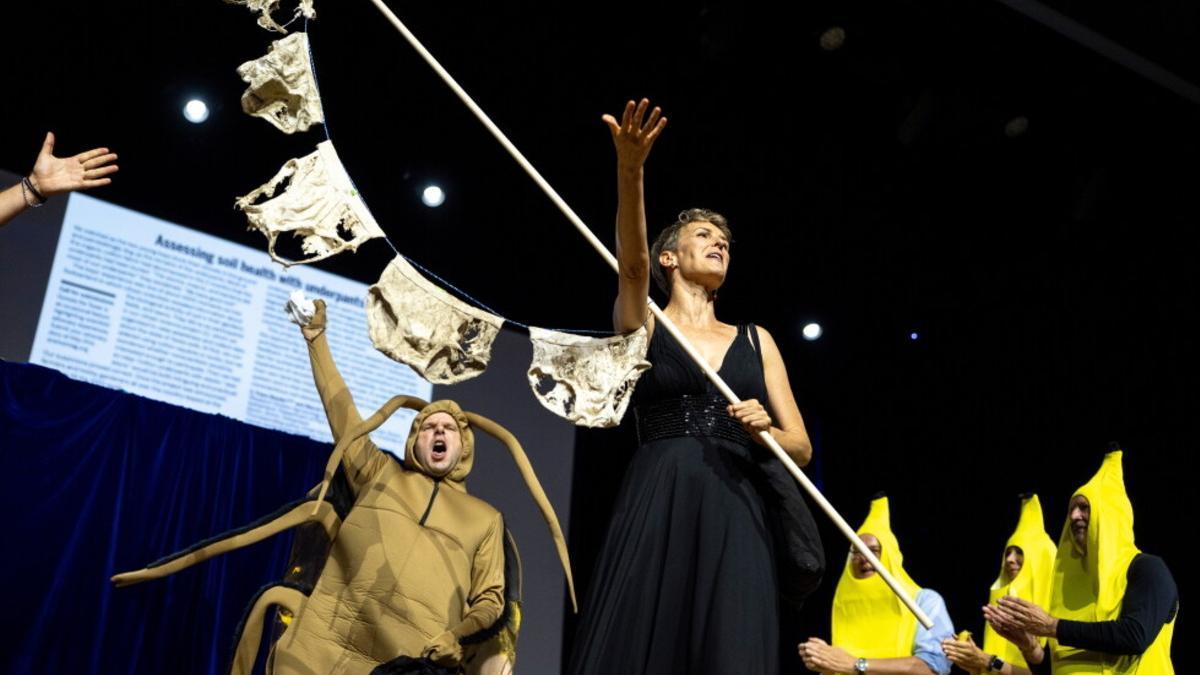 Pia Viviani muestra varias prendas descompuestas durante la entrega del Ig Nobel de Ciencia del Suelo, acompañada por Atlant Bieri y otros participantes de la ceremonia.