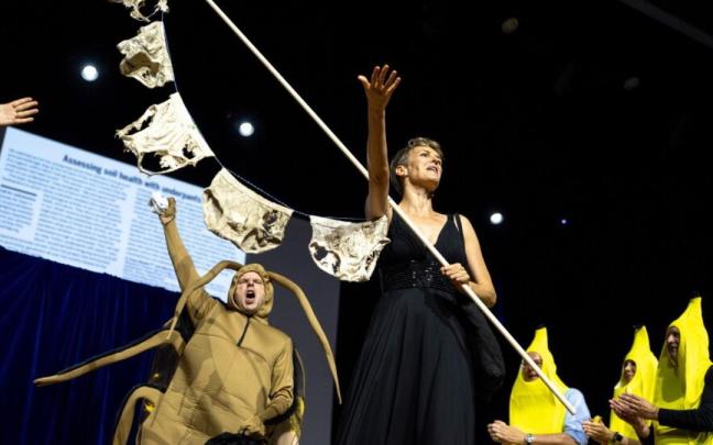 Pia Viviani muestra varias prendas descompuestas durante la entrega del Ig Nobel de Ciencia del Suelo, acompañada por Atlant Bieri y otros participantes de la ceremonia.