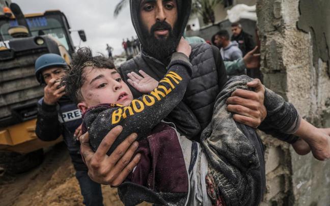 Una persona lleva a un niño herido y rescatado debajo de los escombros de su casa familiar, destruida tras un ataque aéreo israelí contra Deir Al Balah, en el sur de la Franja de Gaza.