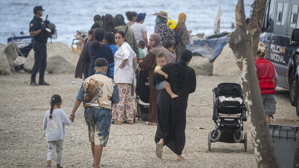 Varios migrantes recogen comida y bebida de Cruz Roja en la playa del Trampolín.