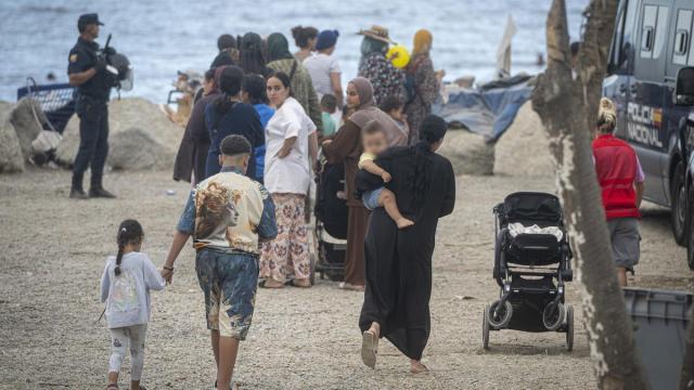Varios migrantes recogen comida y bebida de Cruz Roja en la playa del Trampolín.