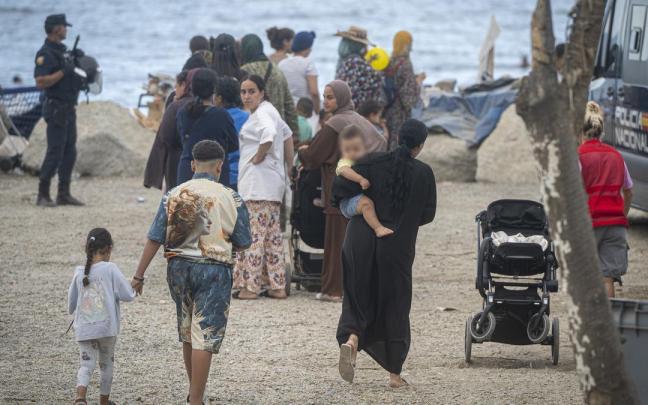 Varios migrantes recogen comida y bebida de Cruz Roja en la playa del Trampolín.