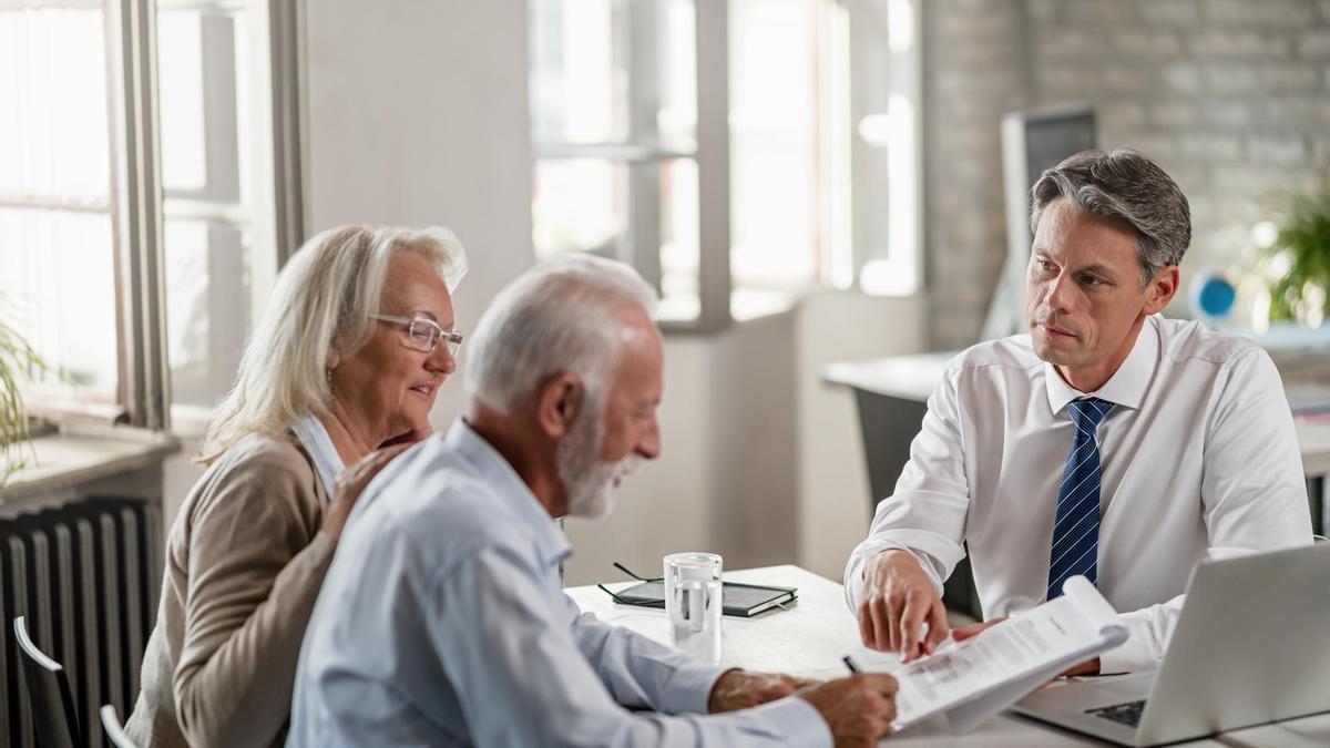 Una pareja mayor firma un contrato en un banco.