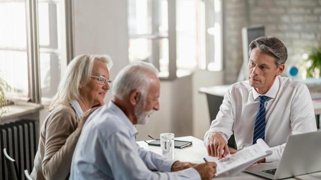 Una pareja mayor firma un contrato en un banco.