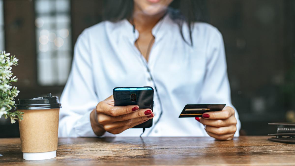 Una mujer compra por internet con su móvil y su tarjeta de crédito.