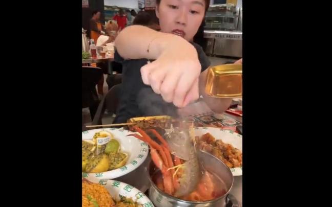 La comensal, tratando de depositar la gamba en la cazuela.