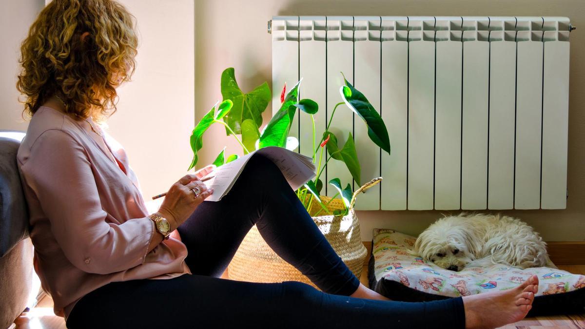 Una mujer repasa un documento cerca de un radiador