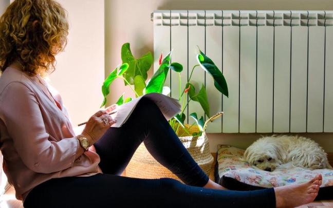 Una mujer repasa un documento cerca de un radiador.