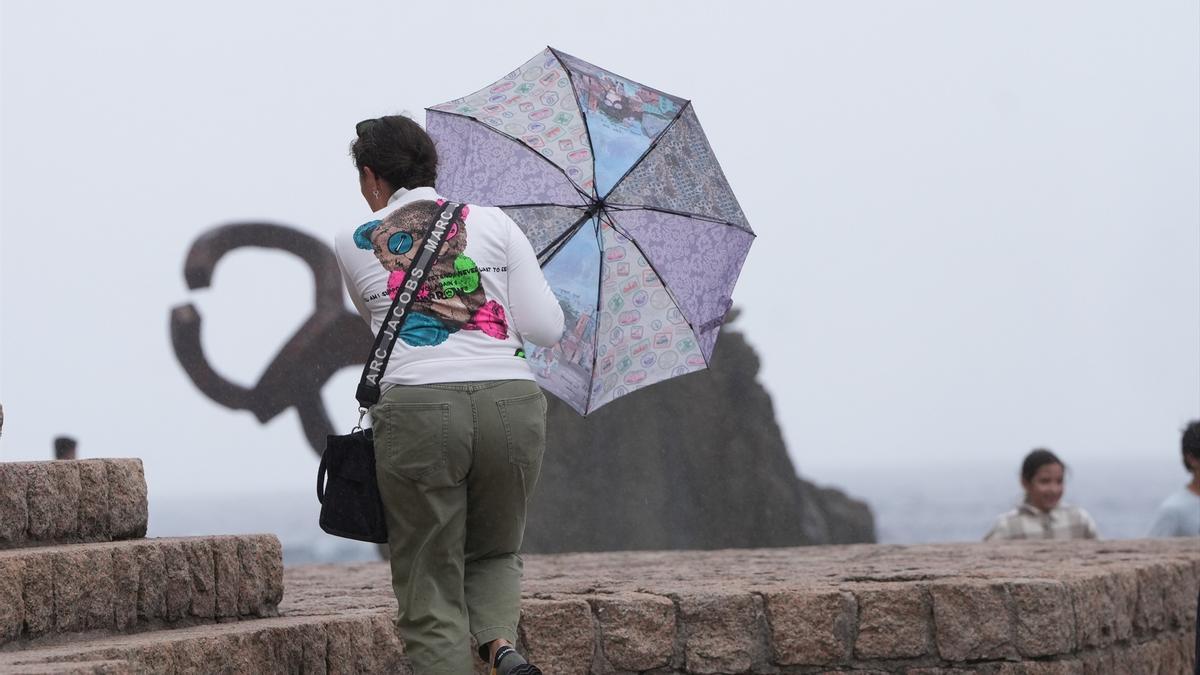 Una mujer camina con un paraguas junto al Peine del Viento.