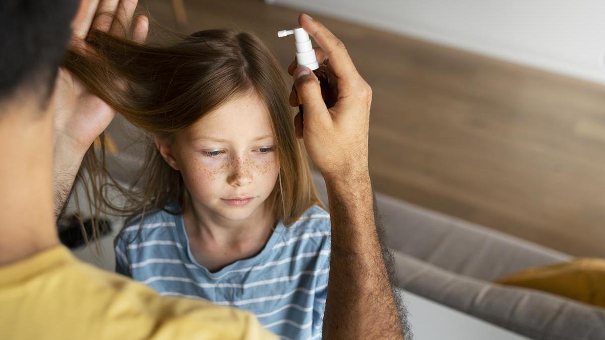 Padre aplica a su hija un producto especial para eliminar los piojos.