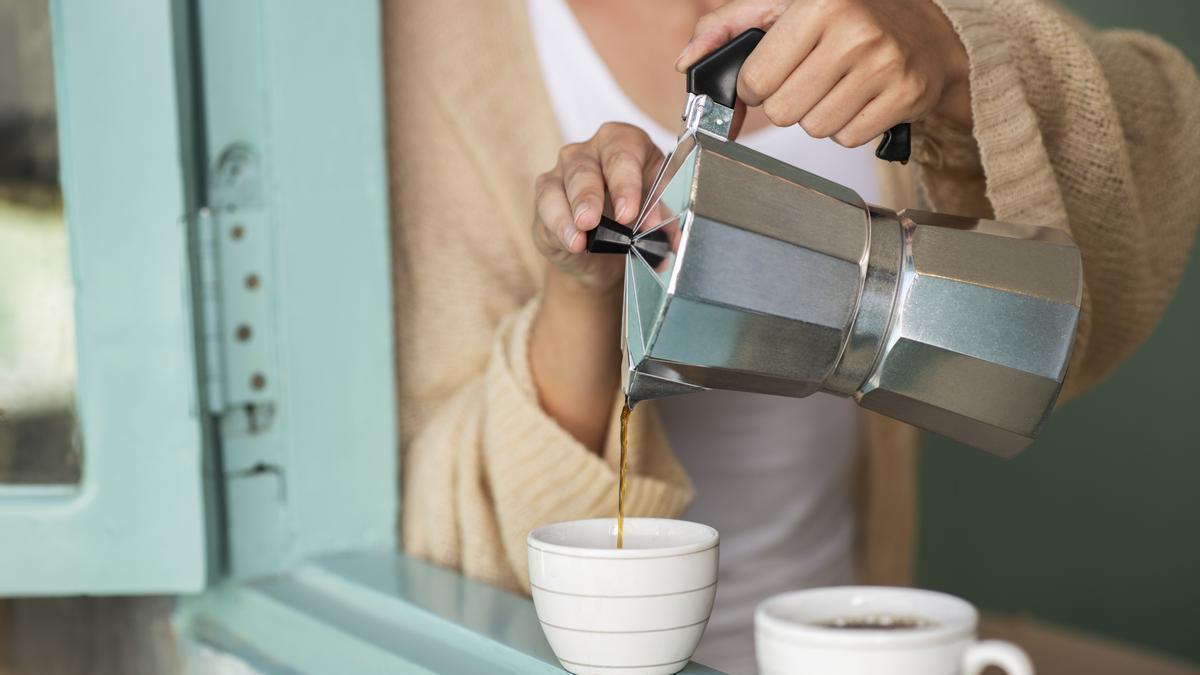 Chica sirve dos tazas de café recién hecho con la cafetera italiana.