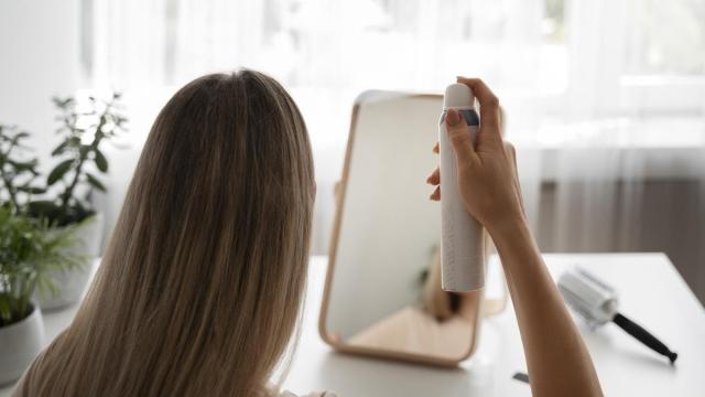 Mujer de espaldas se mira al espejo mientras aplica champú en seco en su cabello.