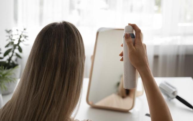 Mujer de espaldas se mira al espejo mientras aplica champú en seco en su cabello.