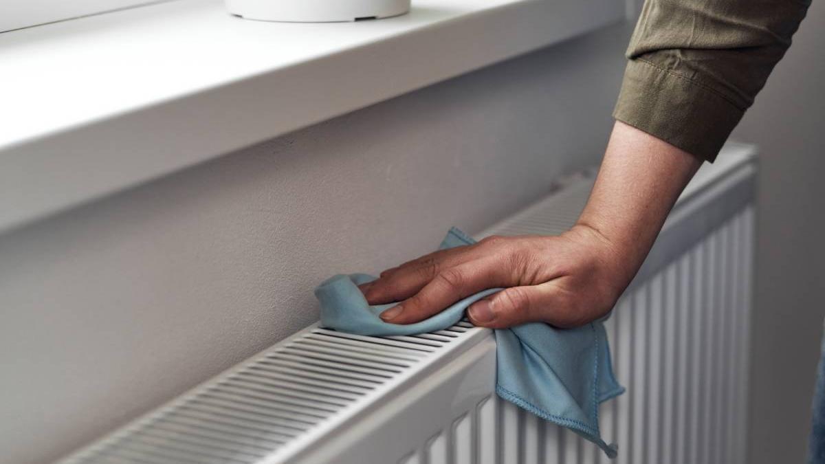 Primer plano de un hombre que limpia un radiador con ayuda de un trapo de microfibra.
