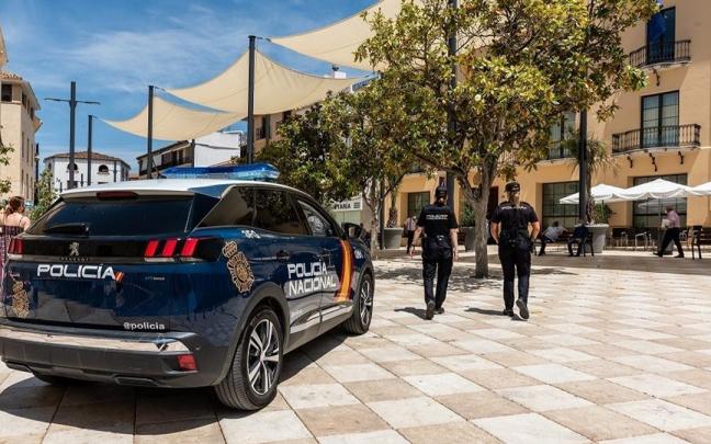 Imagen de archivo de un coche de la Policía Nacional y dos agentes patrullando una calle de Málaga.
