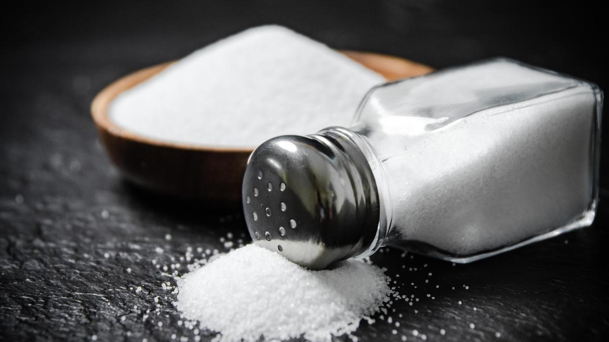Un salero con sal derramada junto a un cuenco lleno de azúcar.