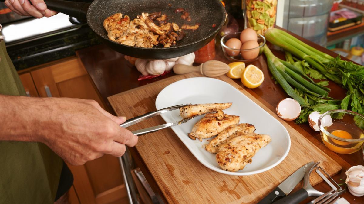 Un cocineroi sirve unas pechugas de pollo recién hechas.