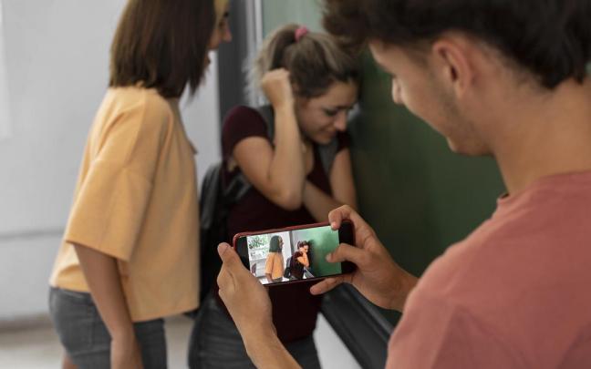 Un joven graba con su móvil como una adolescente acosa a una compañera de clase.