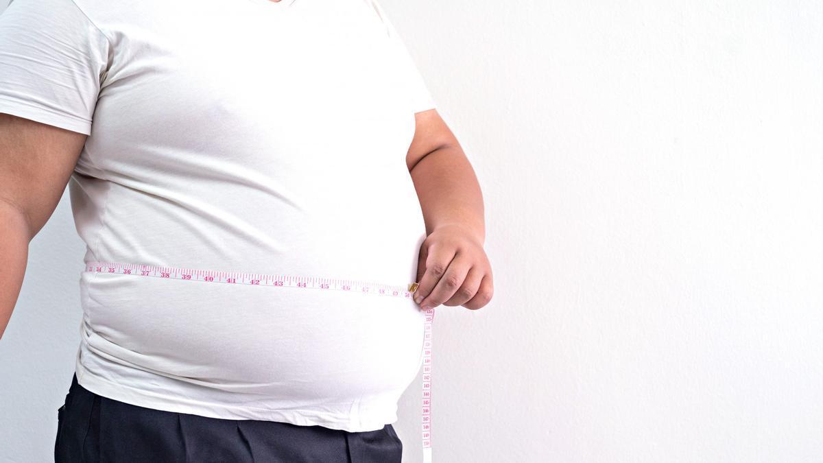 Un hombre obeso mide su abdomen con una cinta métrica.