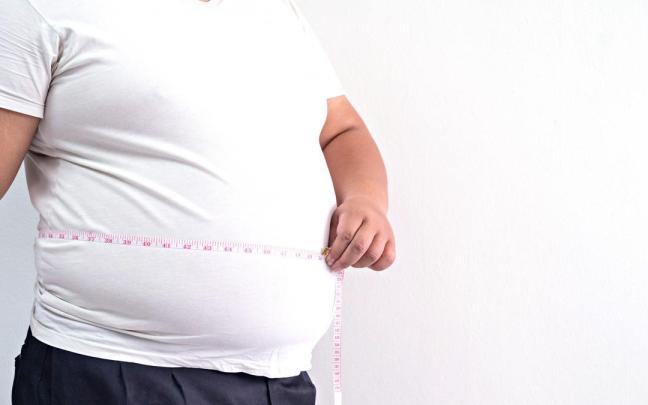 Un hombre obeso mide su abdomen con una cinta métrica.