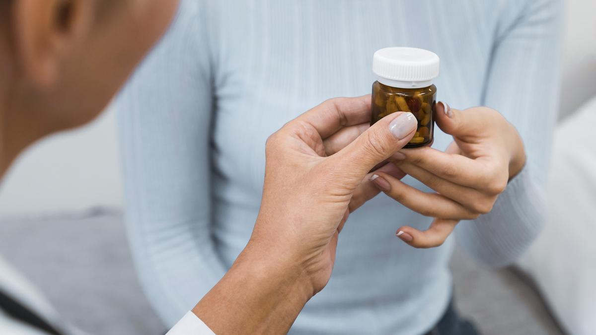 Una farmacéutica entrega a una mujer un bote de medicamentos.