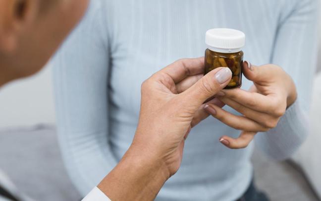 Una farmacéutica entrega a una mujer un bote de medicamentos.