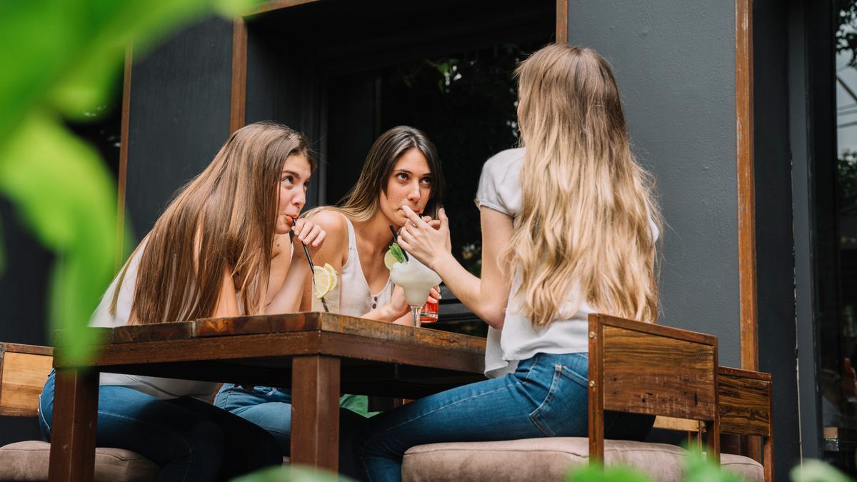 Tres amigas comparten mesa y confidencias en una terraza.