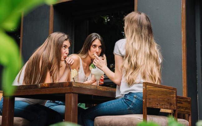 Tres amigas comparten mesa y confidencias en una terraza.