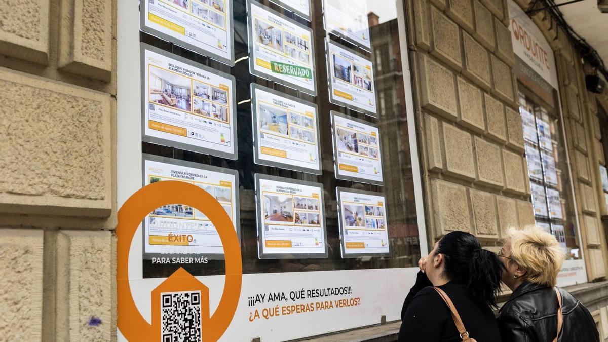 Dos mujeres observan precios de pisos en una inmobiliaria.