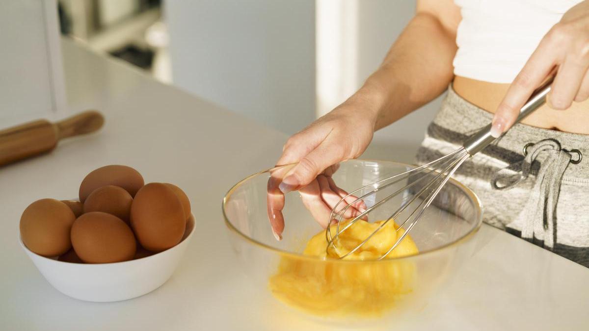 Chica bate huevos en un bol para preparar una receta