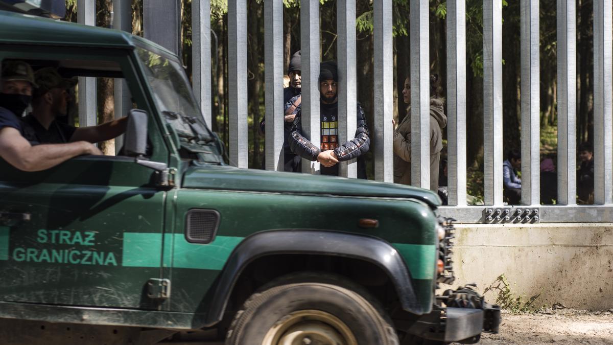 Guardias fronterizos polacos pasan junto a los migrantes que permanecen en el lado bielorruso del muro fronterizo.