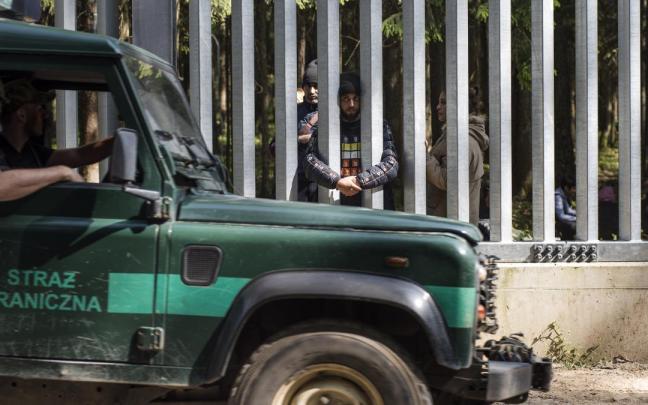 Guardias fronterizos polacos pasan junto a los migrantes que permanecen en el lado bielorruso del muro fronterizo. Guardias fronterizos polacos pasan junto a los migrantes que permanecen en el lado bielorruso del muro fronterizo.