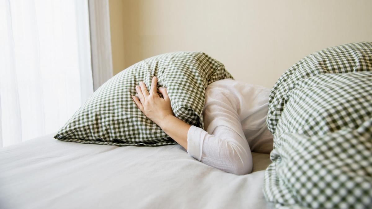 Una mujer se cubre la cabeza con la almohada.