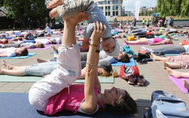 Una mujer comparte ejercicios de yoga con su hijo en una sesion conjunta con otras mujeres.