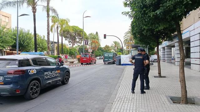 Un vehículo de la Policía Nacional y dos agentes en la zona acordonada donde ha aparecido un cadáver en un contenedor en Jerez.