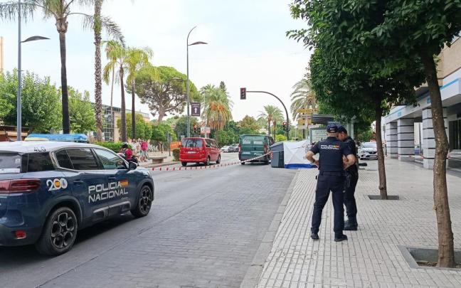 Un vehículo de la Policía Nacional y dos agentes en la zona acordonada donde ha aparecido un cadáver en un contenedor en Jerez.