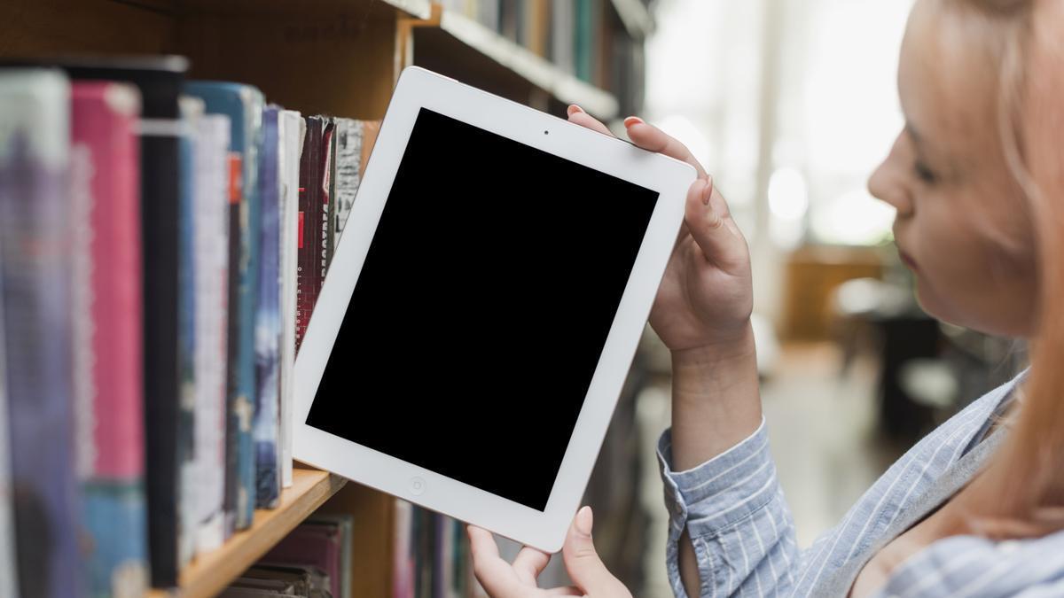 Una joven saca un e-book de la estantería de una biblioteca.