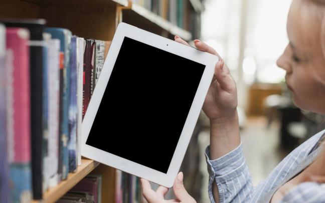 Una joven saca un e-book de la estantería de una biblioteca.